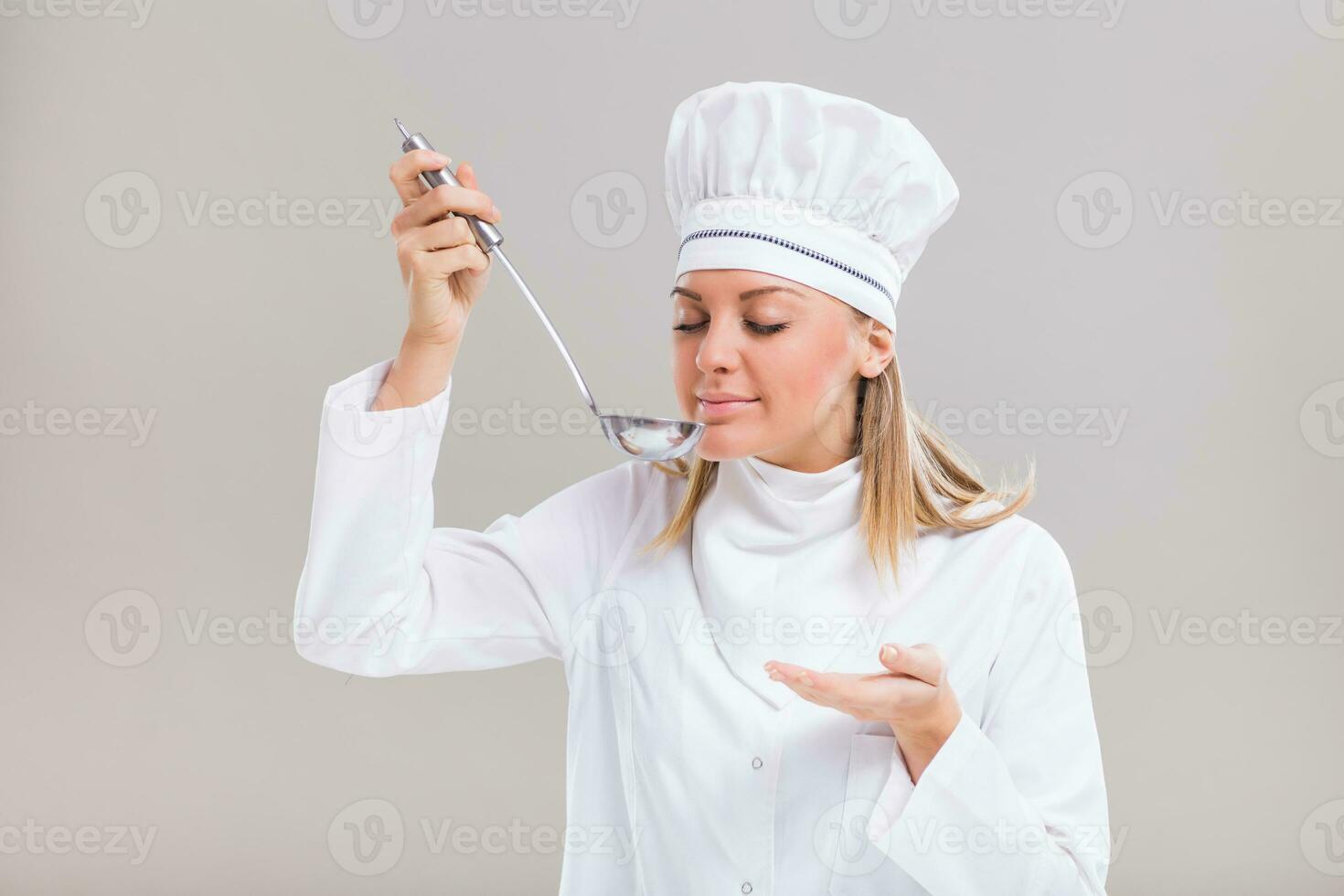 Beautiful female chef has made tasteful soup and she is smelling it. photo