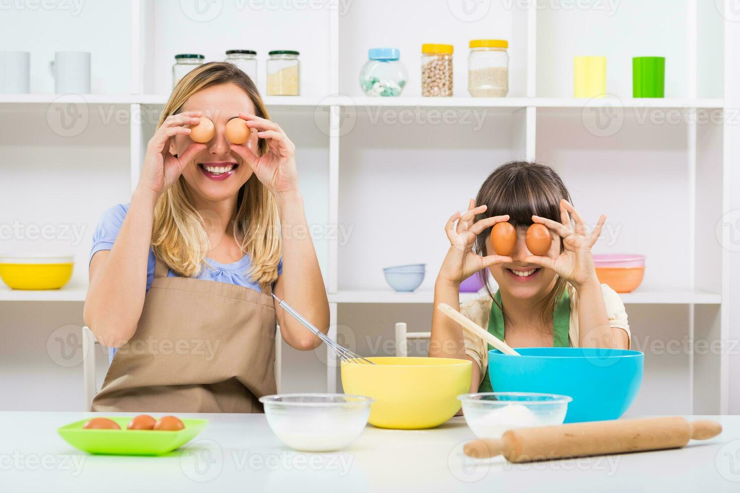 Happy mother and her daughter are covering their eyes with eggs,they are having fun while making cookie. photo