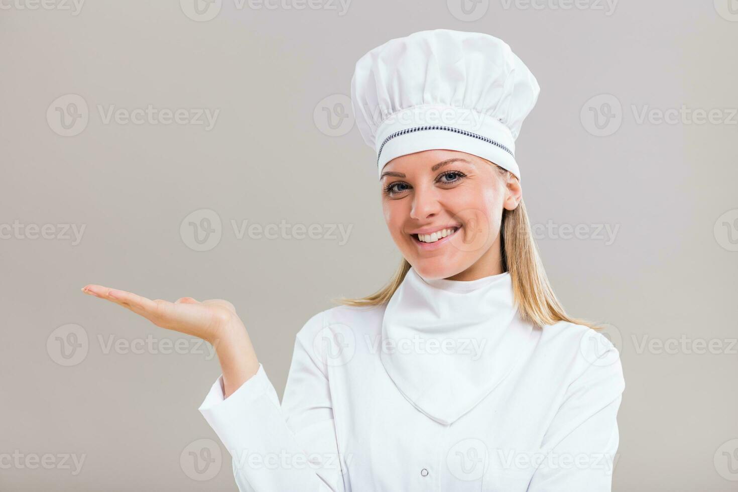 Portrait of beautiful female chef gesturing on gray background. photo