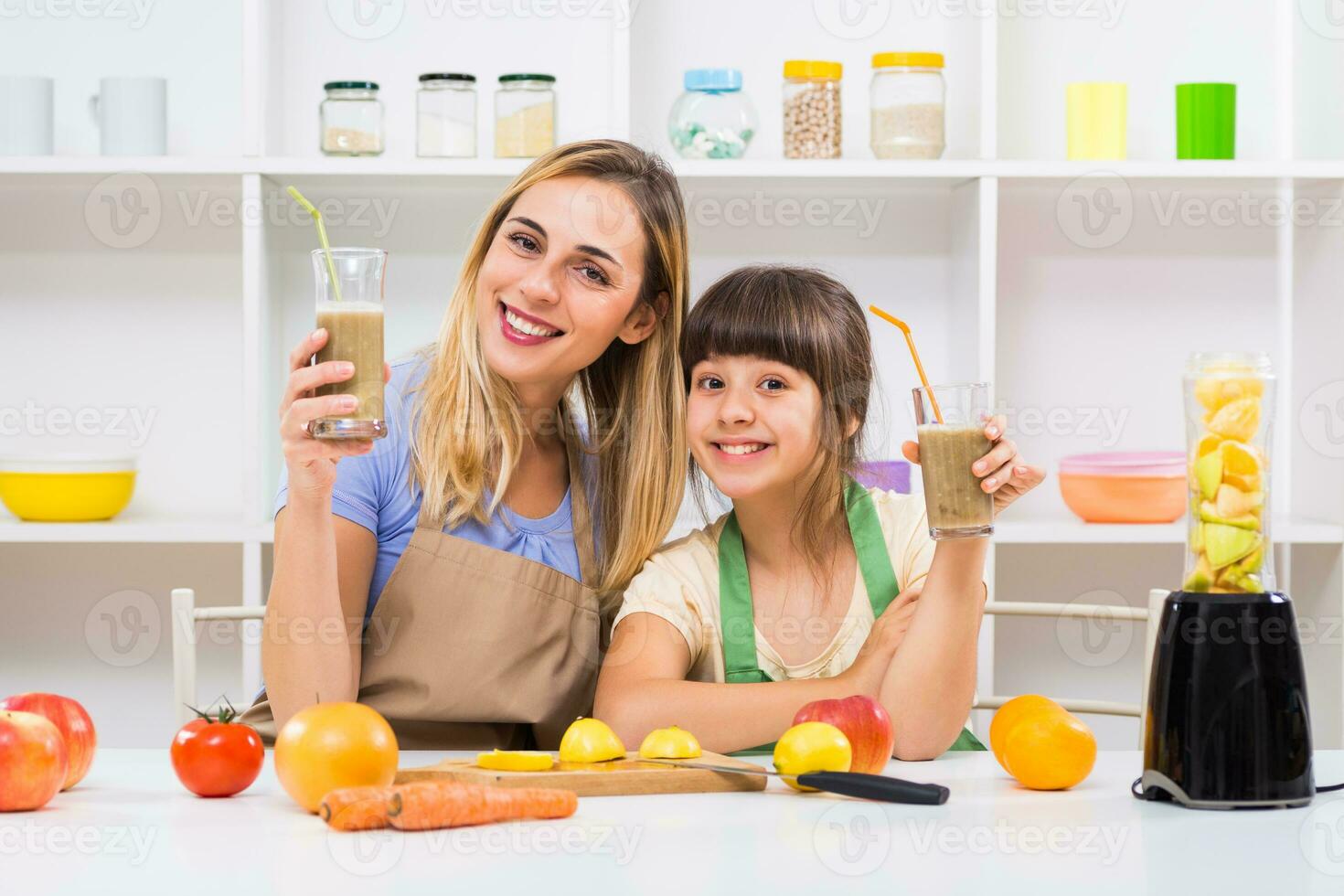 Happy mother and her daughter enjoy making and drinking smoothies together at their home. photo