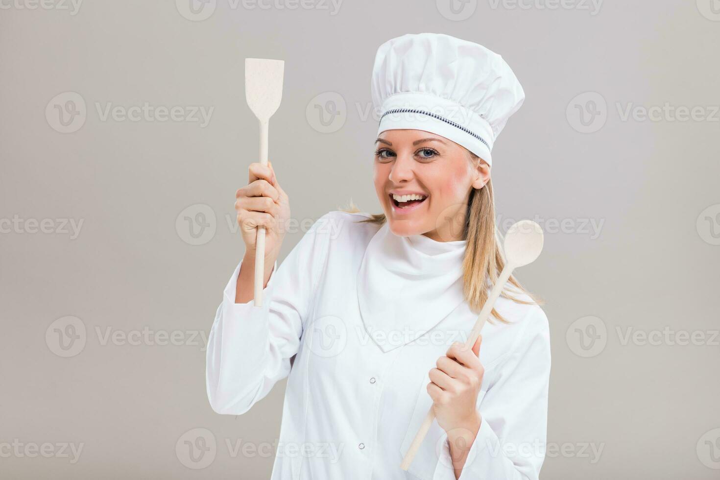Happy female chef holding her work tool on gray background. photo