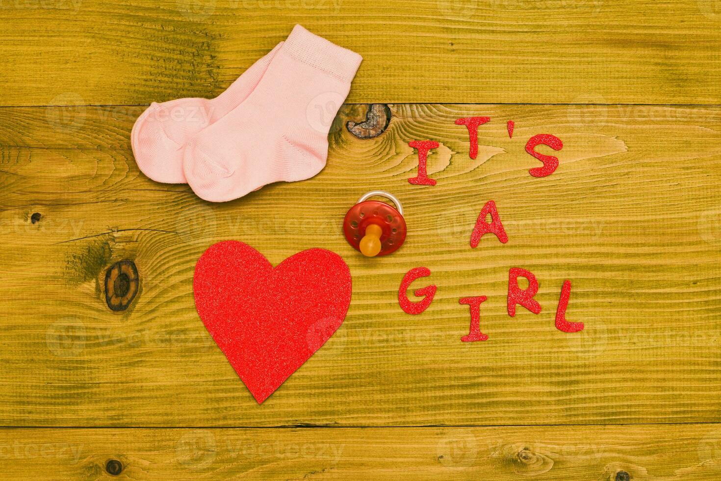 Text it's a girl with baby supplies and heart shape  on wooden table photo