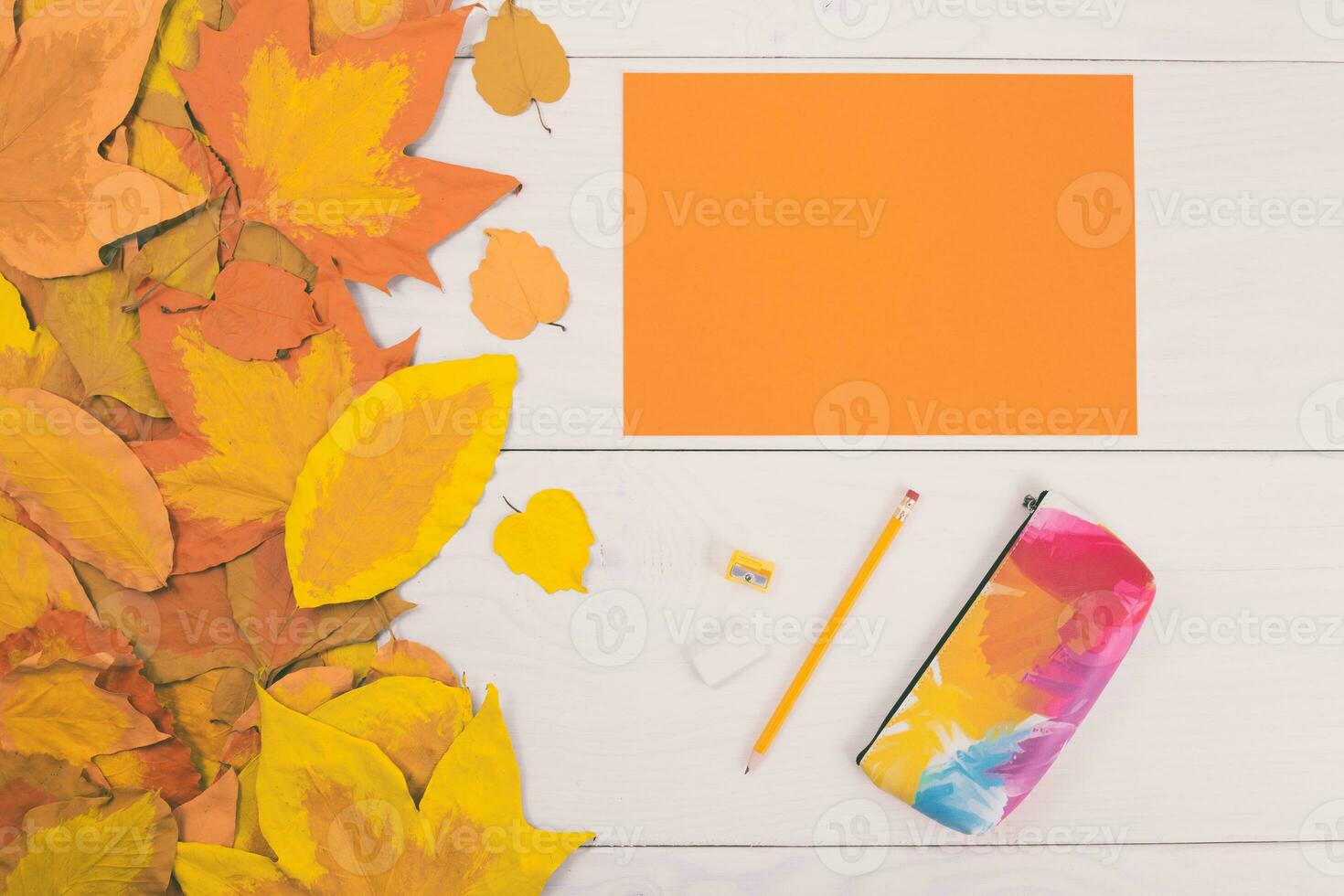 Autumn leaves and orange paper and school supplies on white wooden background photo