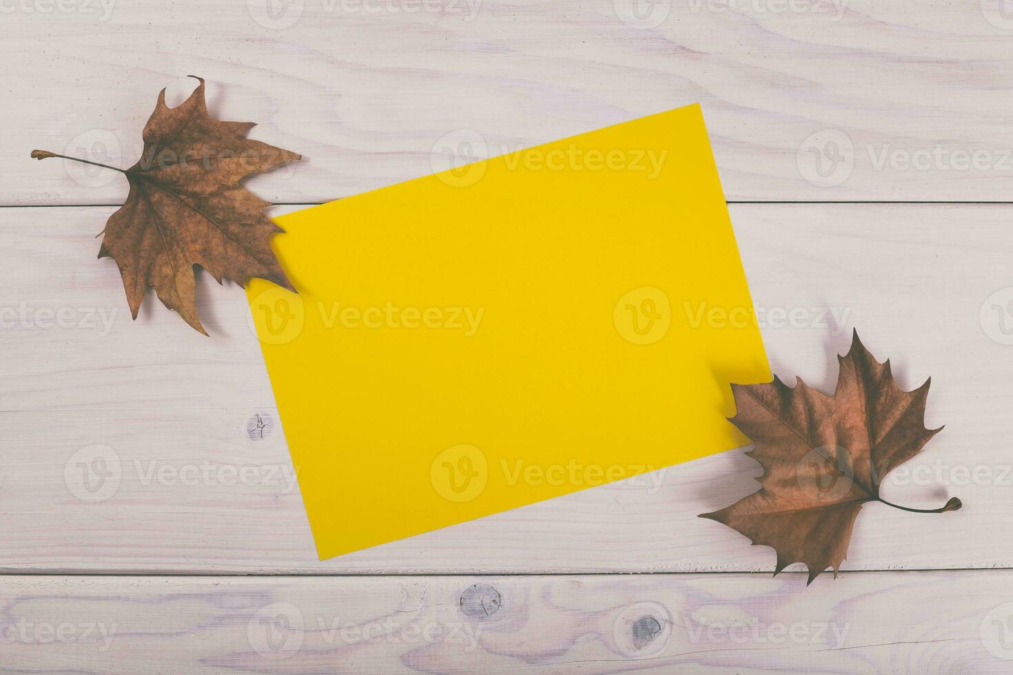 Yellow paper on wooden background with autumn leaves photo