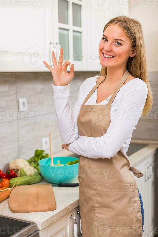 Beautiful woman showing ok sign while making meal in her kitchen photo