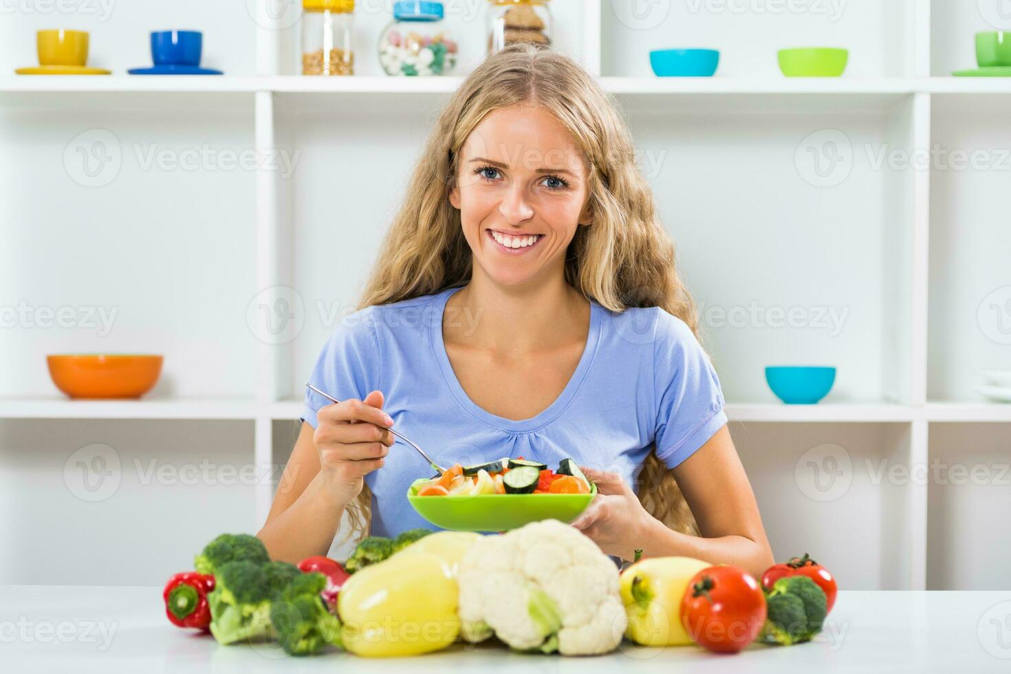 Beautiful girl enjoys eating vegetable salad at her home photo