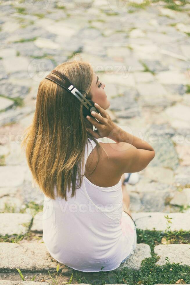 joven mujer disfruta escuchando música mientras sentado en el escalera en el ciudad. foto