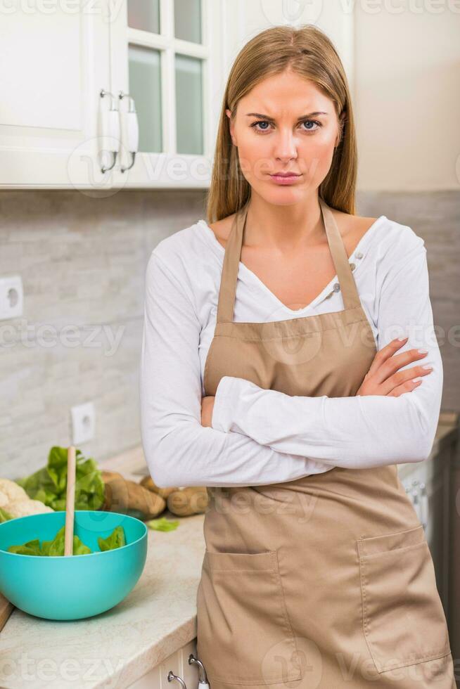 enojado mujer en pie en su cocina mientras haciendo comida foto