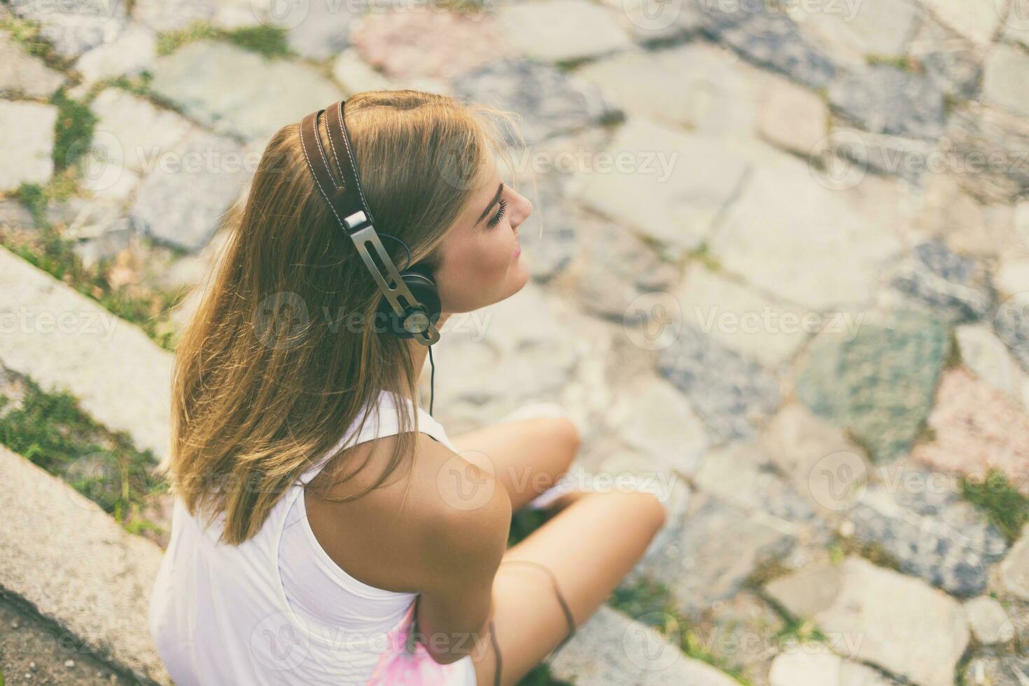 joven mujer disfruta escuchando música mientras sentado en el escalera en el ciudad. foto