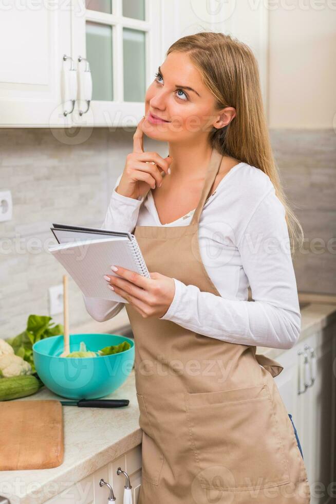 Beautiful woman reading cookbook while making a meal photo