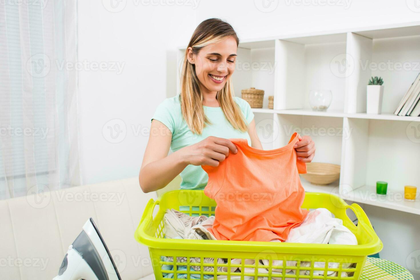 Beautiful woman with clothes in basket and iron at her home photo