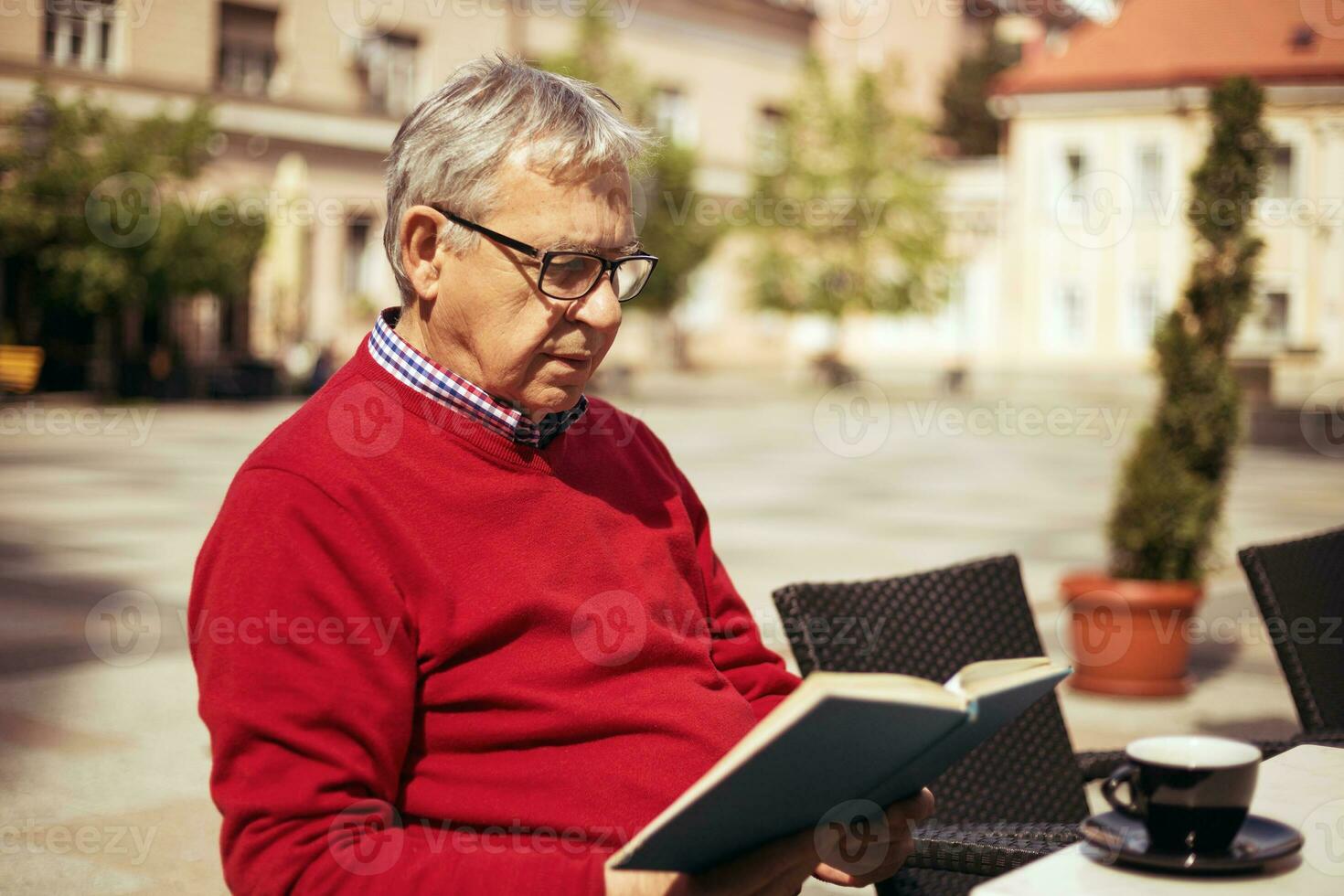 Senior man enjoys reading book and drinking coffee at the bar photo