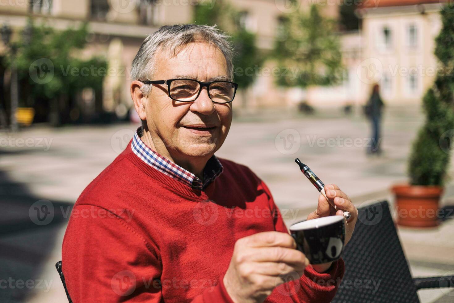 Cheerful senior man enjoys drinking coffee and smoking electronic cigarette at the bar photo