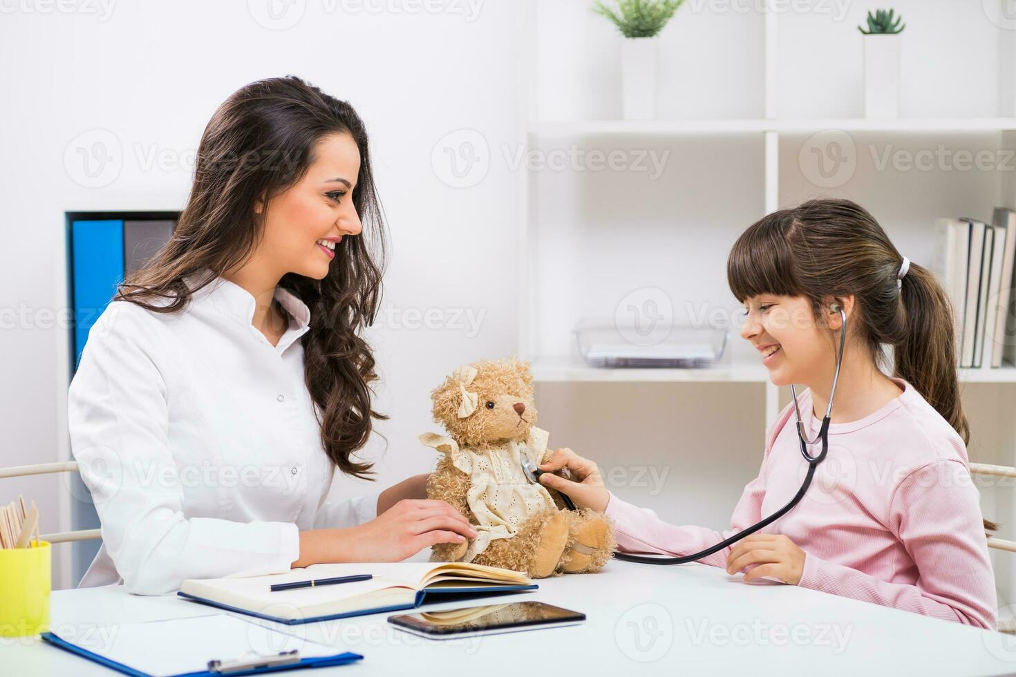 Female doctor and little girl examining teddy bear at medical office photo
