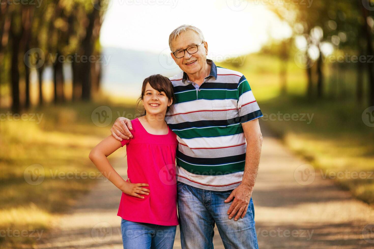 Portrait of happy grandfather and granddaughter standing in nature photo