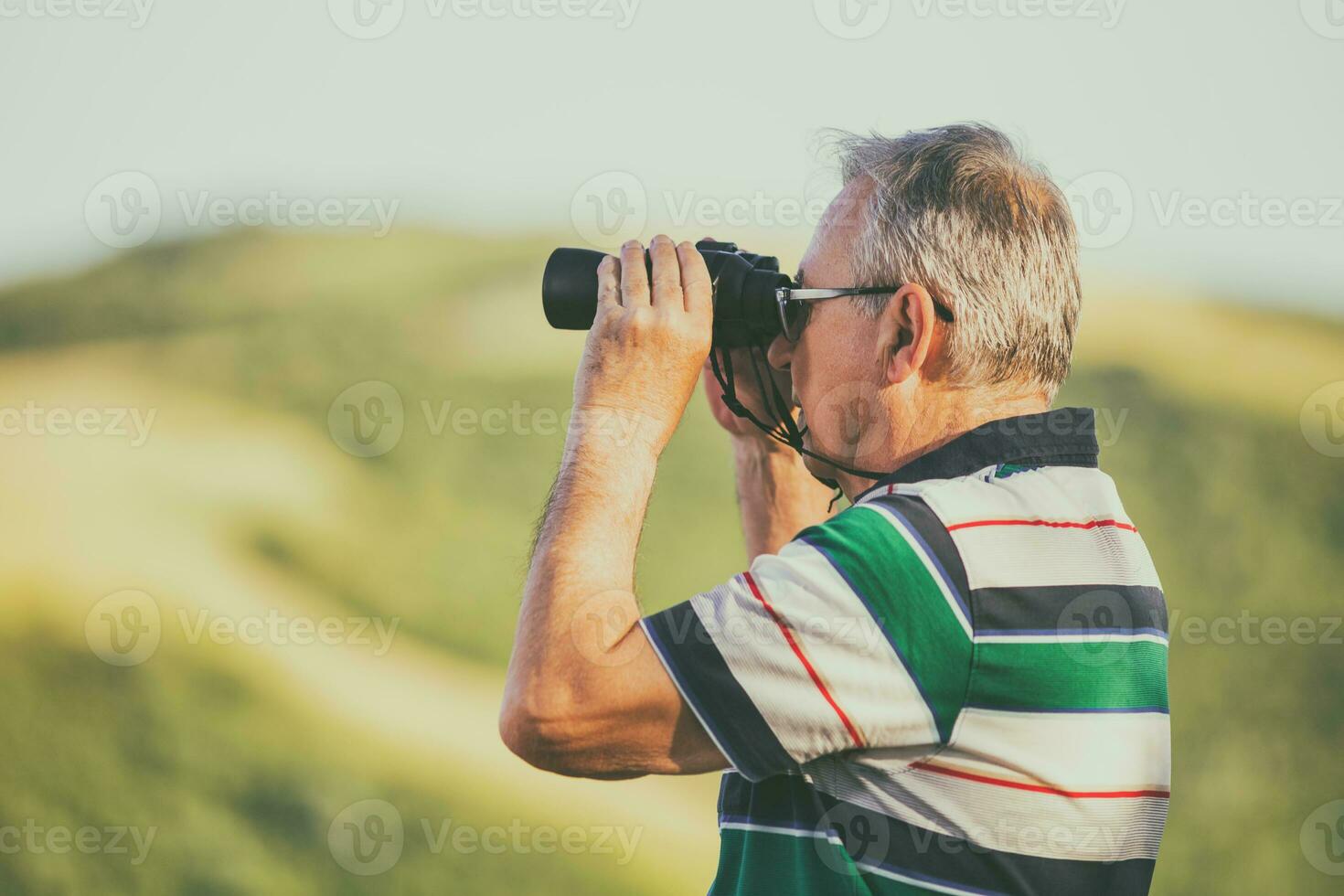 Senior man enjoys looking through binoculars in the nature photo