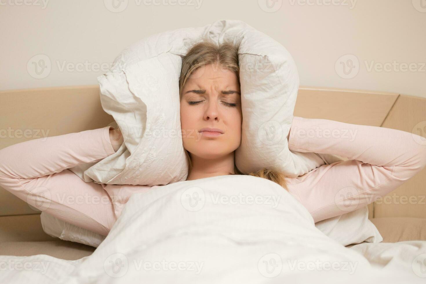 Angry woman disturbed with a noise trying to sleep and covering her ears with a pillow photo