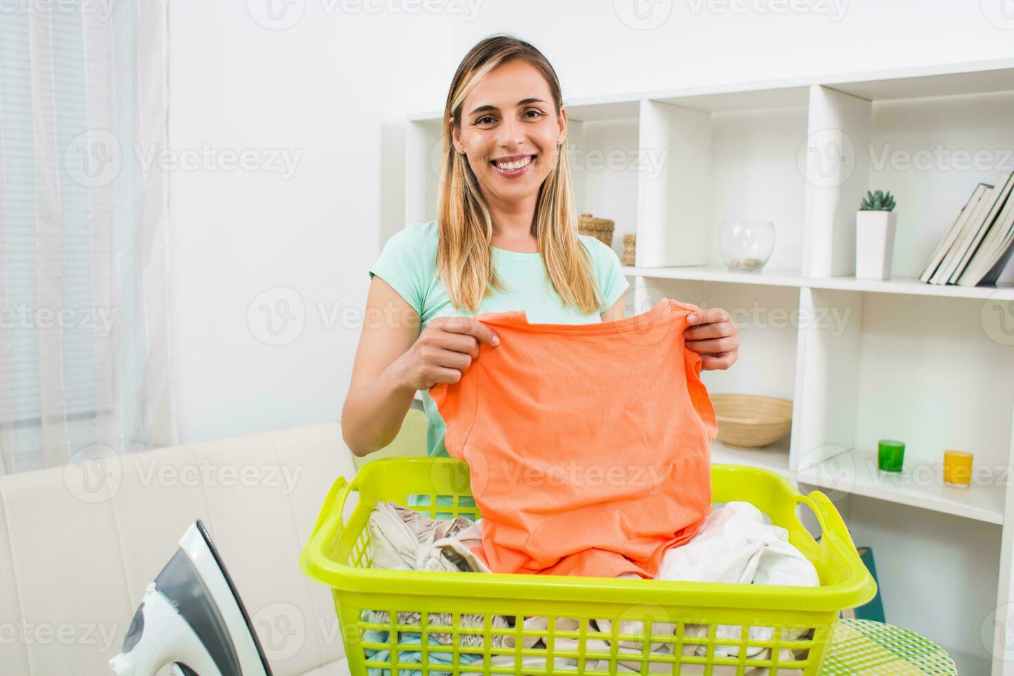 Beautiful woman with clothes in basket and iron at her home photo