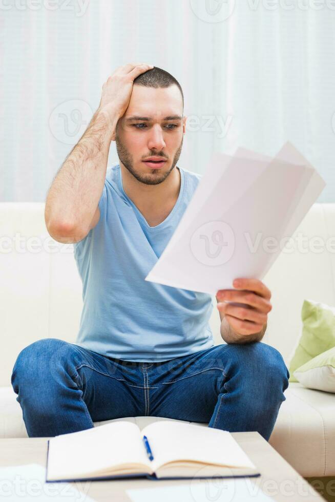 Young man looking at his document in panic while working at his home photo