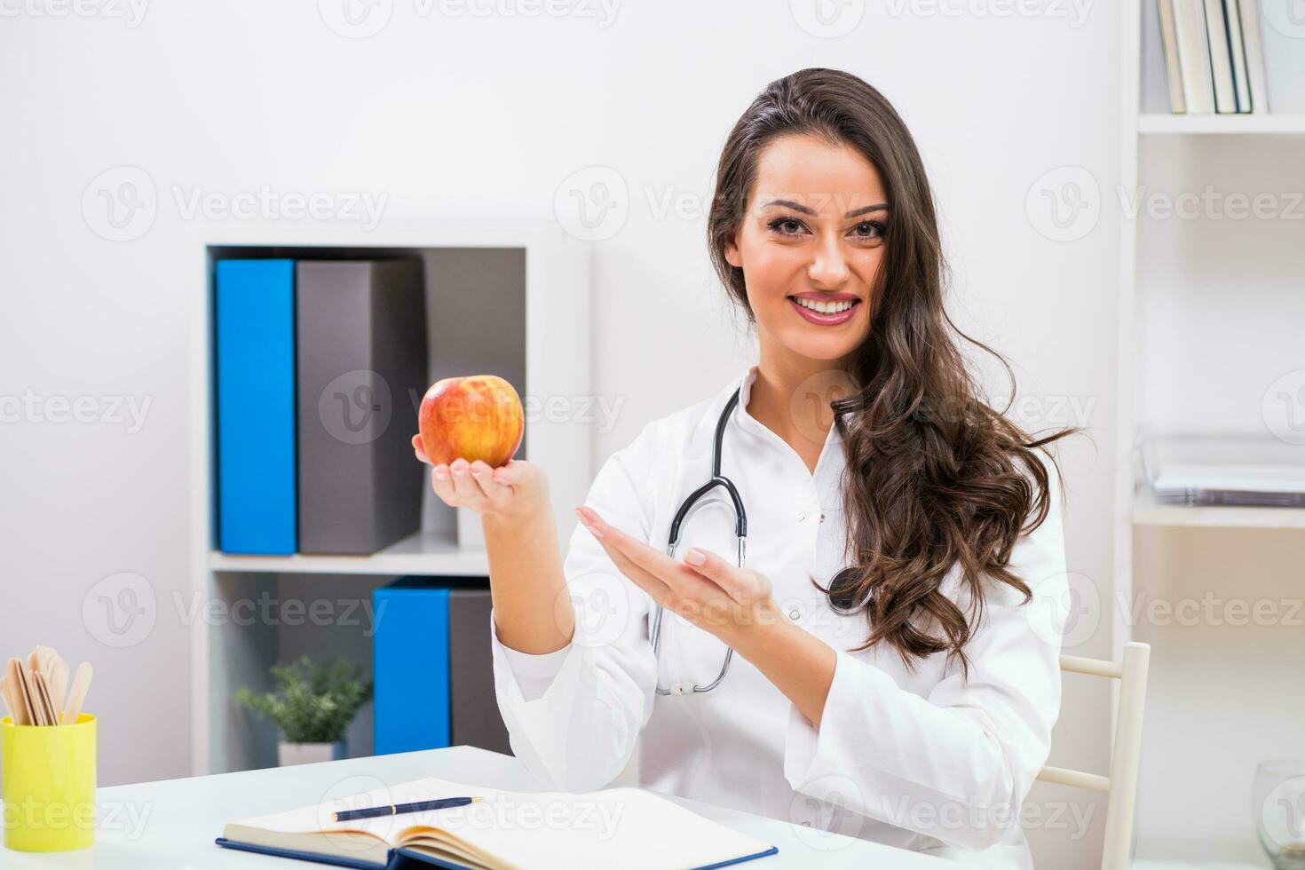 Beautiful female doctor showing apple while working at her office photo