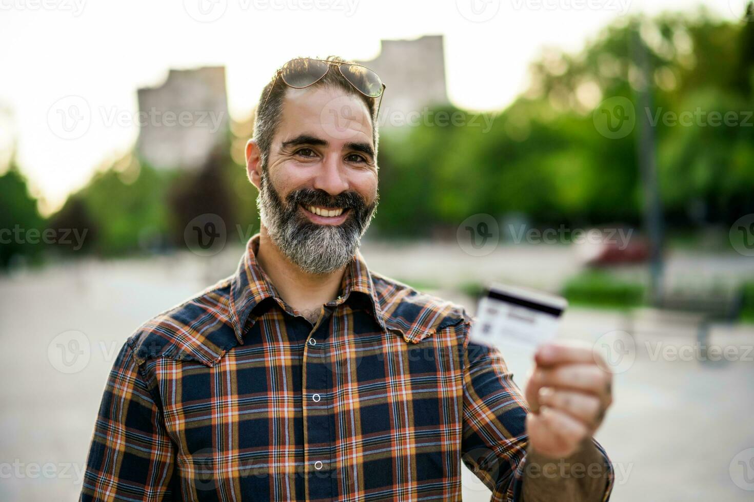 retrato de moderno empresario con barba participación crédito tarjeta mientras en pie en el ciudad calle foto