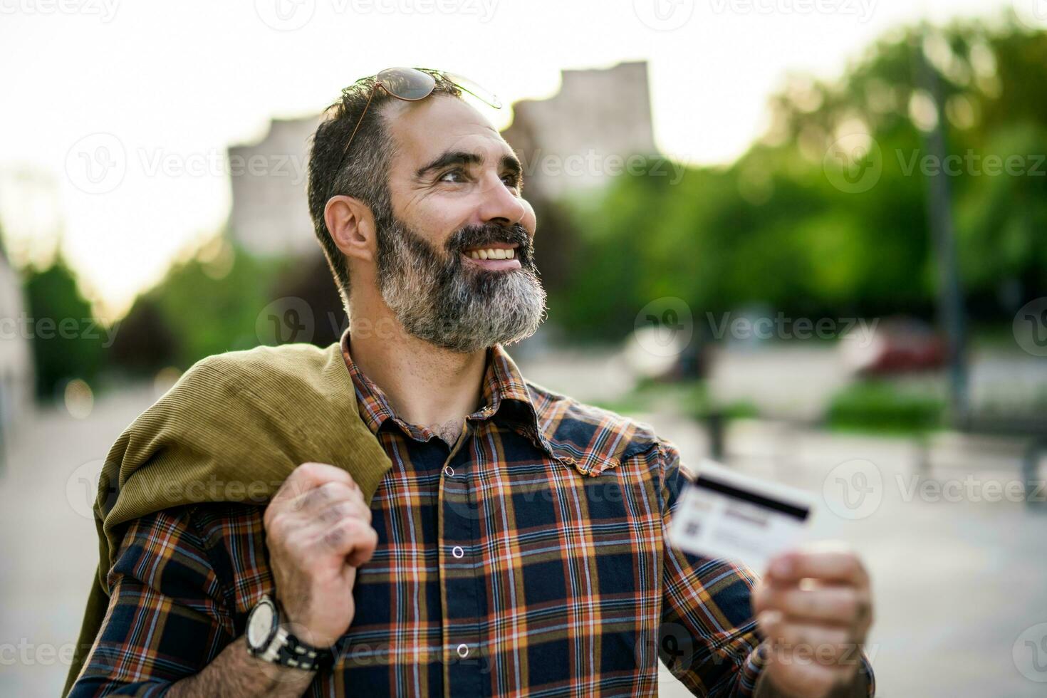Portrait of modern businessman with beard holding credit card while standing on the city street photo