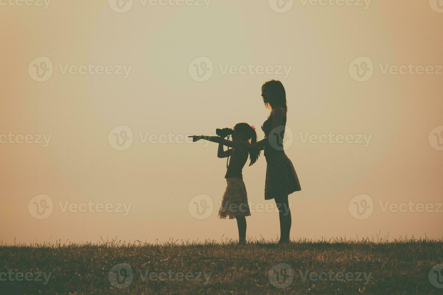 pequeño niña es en pie con su madre al aire libre y acecho con prismáticos naturaleza foto