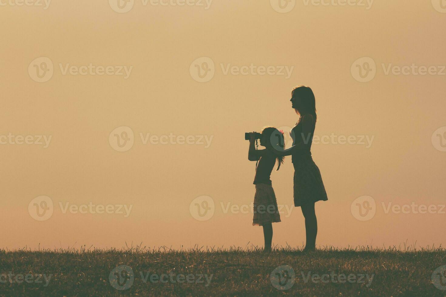 Little girl is standing with her mother outdoor and watching with binoculars nature. photo