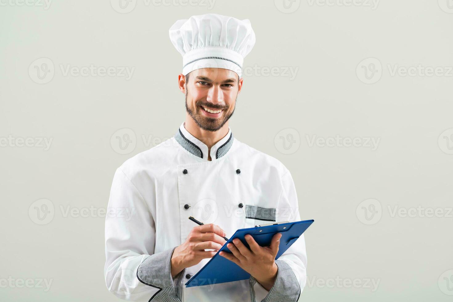 Smiling chef is holding cookbook and writing a new recipe. photo