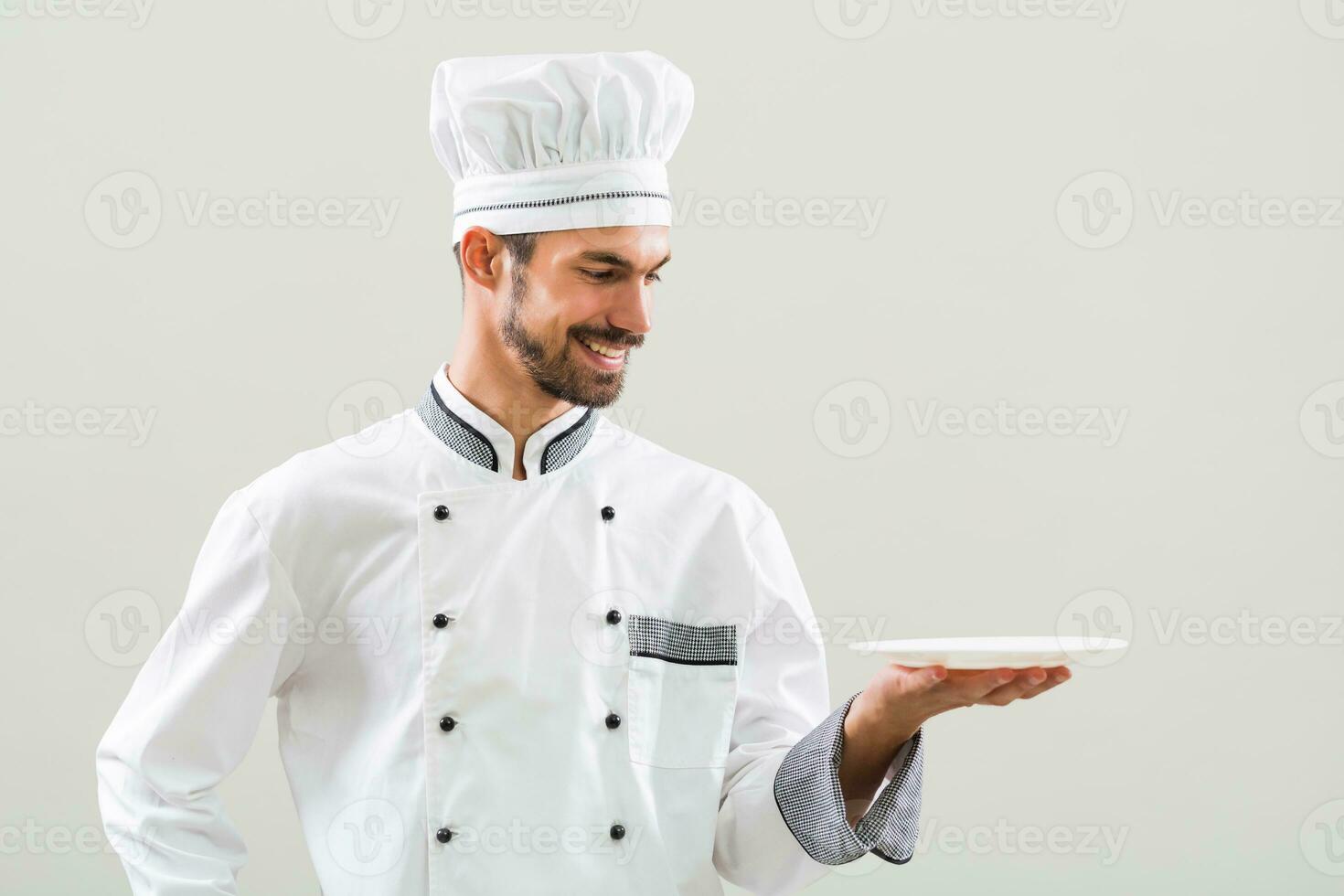 Smiling chef is holding plate and  on gray background. photo