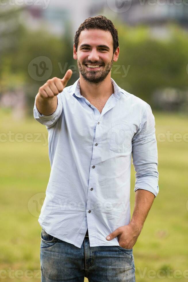 Young businessman is standing in the park and showing thumb uP photo