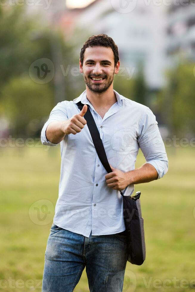 Young businessman is standing in the park and showing thumb up photo