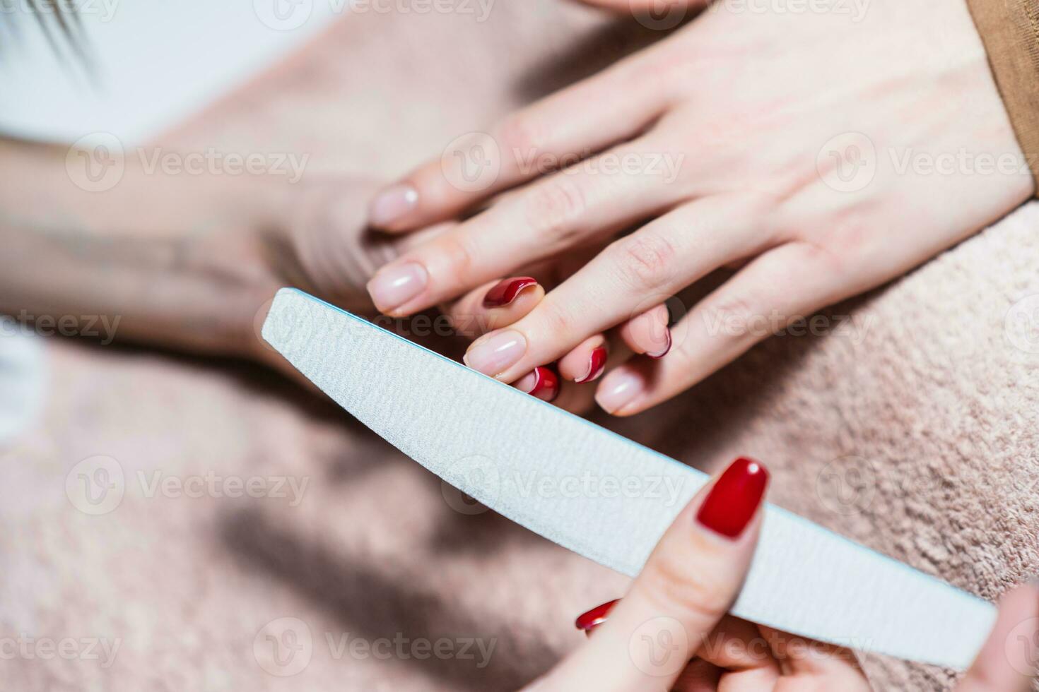 Close up image of manicure process, manicurist using nail file on female fingernails. Focus on fingernail. photo