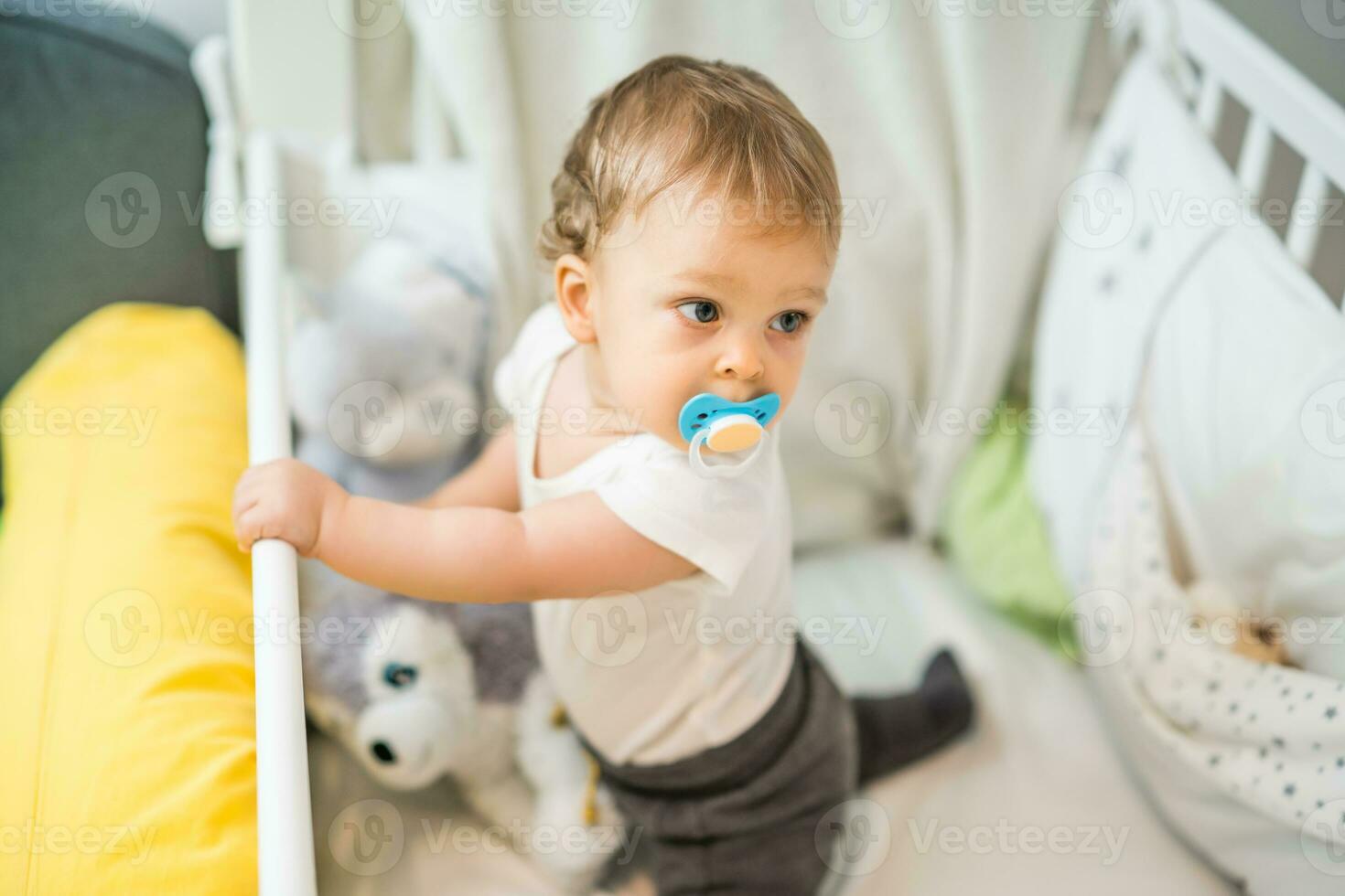 Image of cute baby boy with pacifier sitting in crib photo