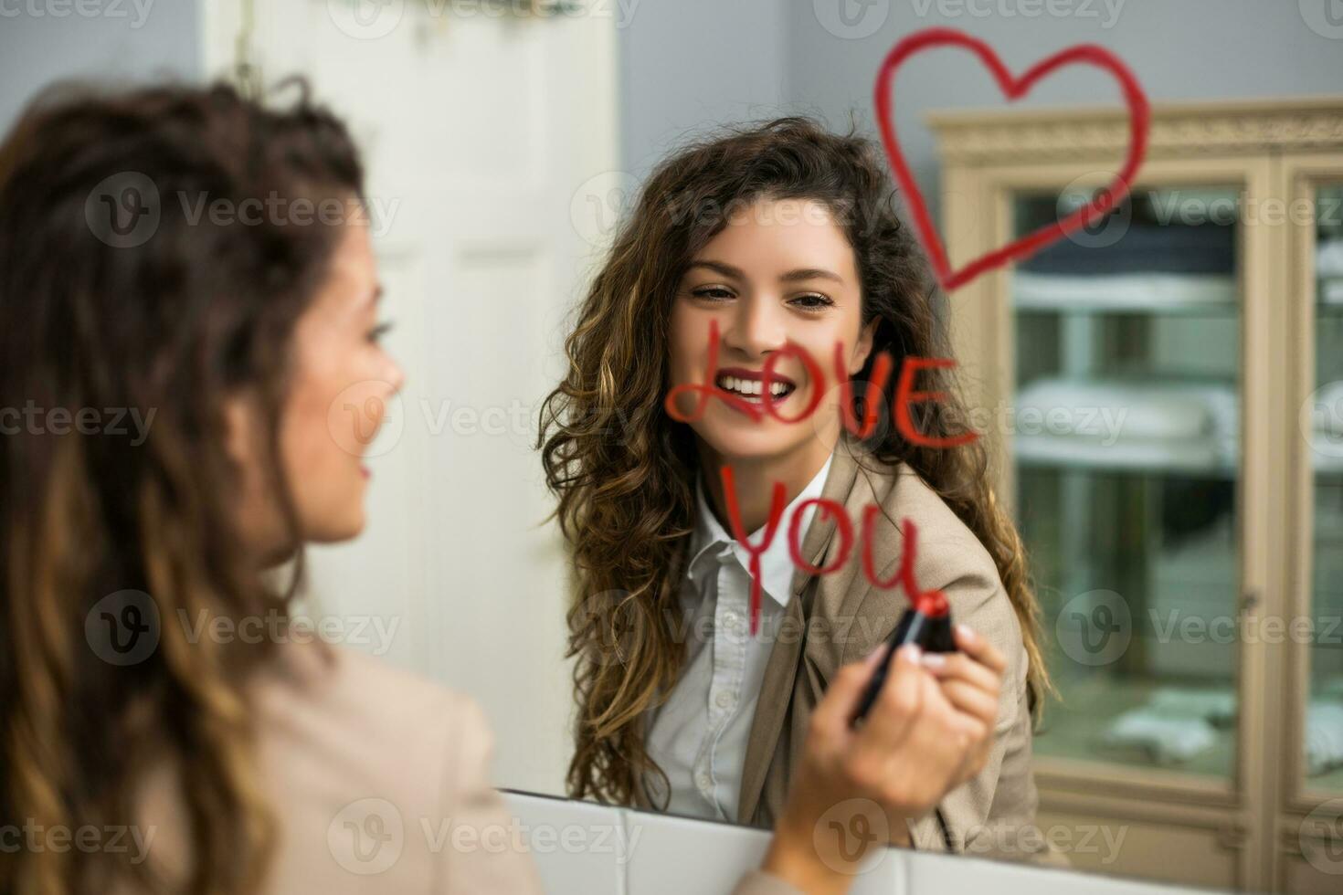 mujer de negocios es dibujo corazón y escritura yo amor usted con lápiz labial en el espejo mientras preparando para trabajo foto