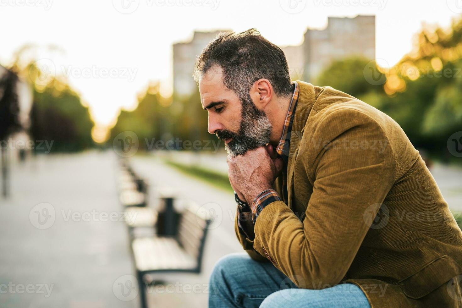 Deprimido empresario con barba sentado en el banco en el ciudad foto