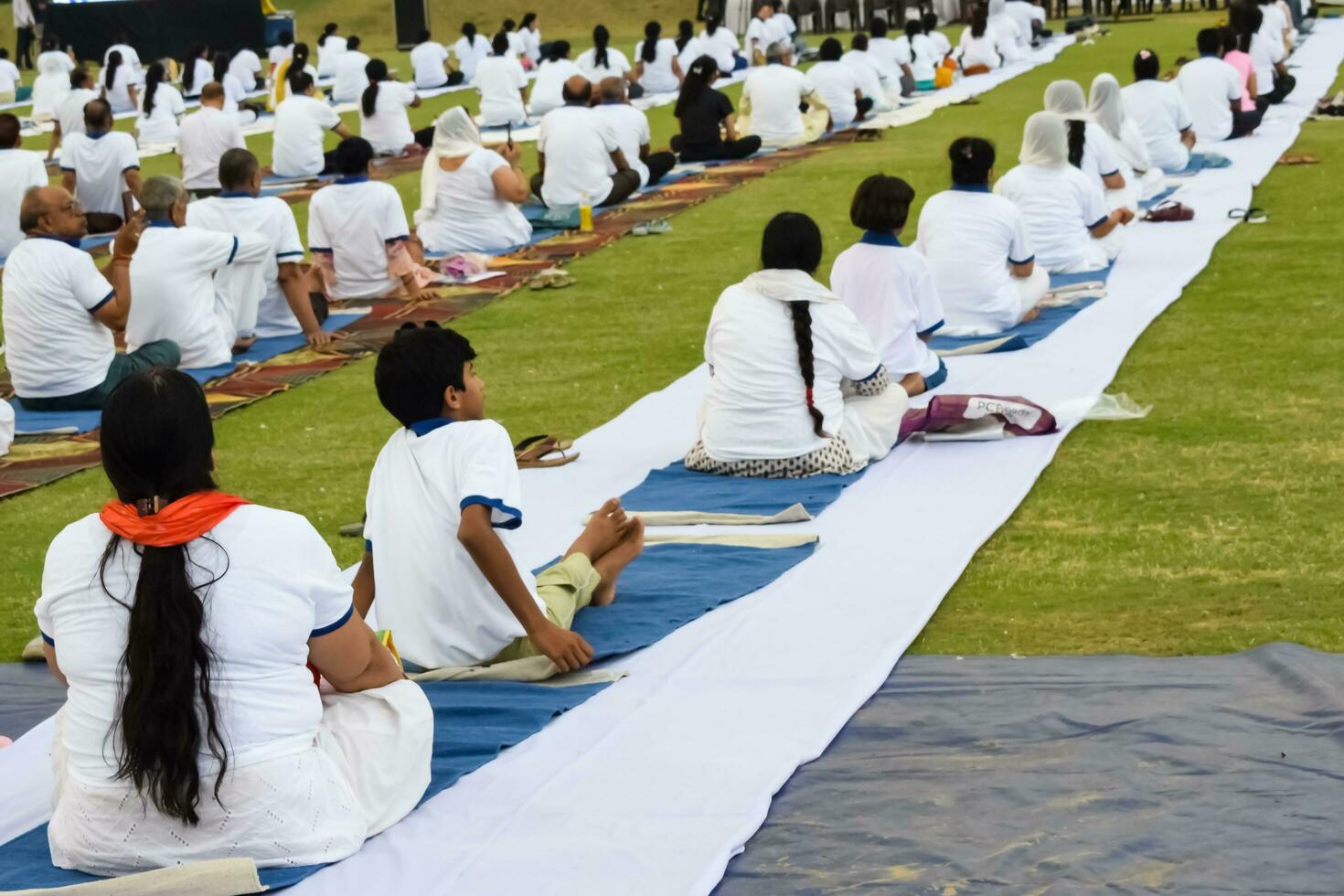 New Delhi, India, June 21, 2023 - Group Yoga exercise session for people at Yamuna Sports Complex in Delhi on International Yoga Day, Big group of adults attending yoga class in cricket stadium photo