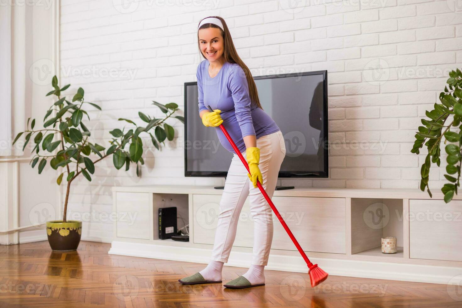 Beautiful pregnant woman enjoys cleaning her house. photo