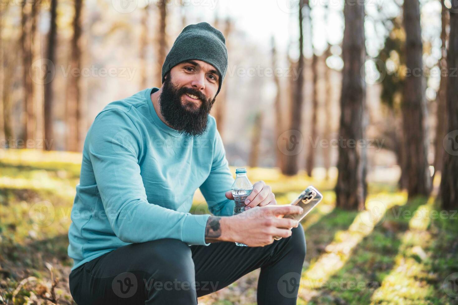 Man using phone and drinking water after exercise in the nature photo
