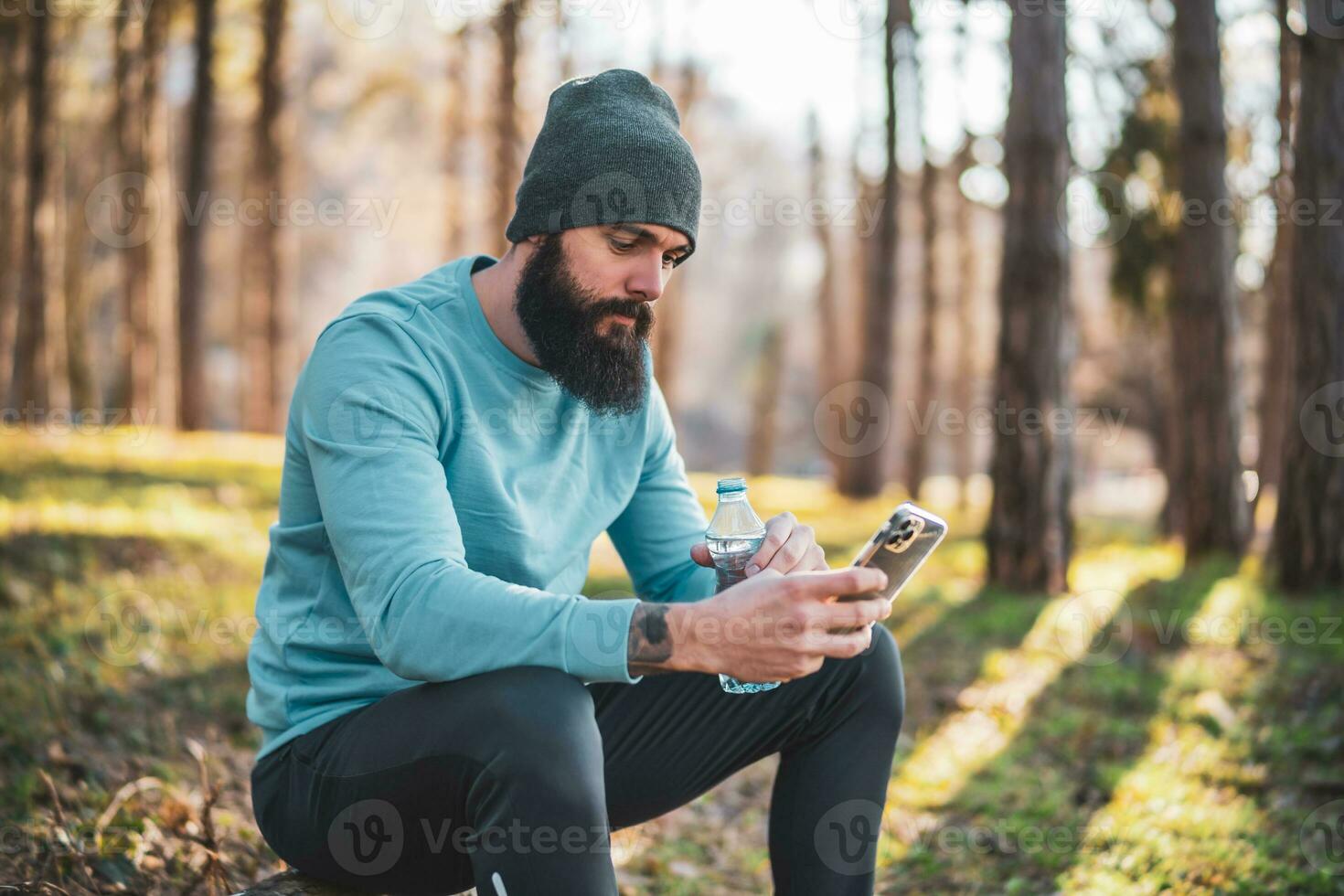 Man using phone and drinking water after exercise in the nature photo