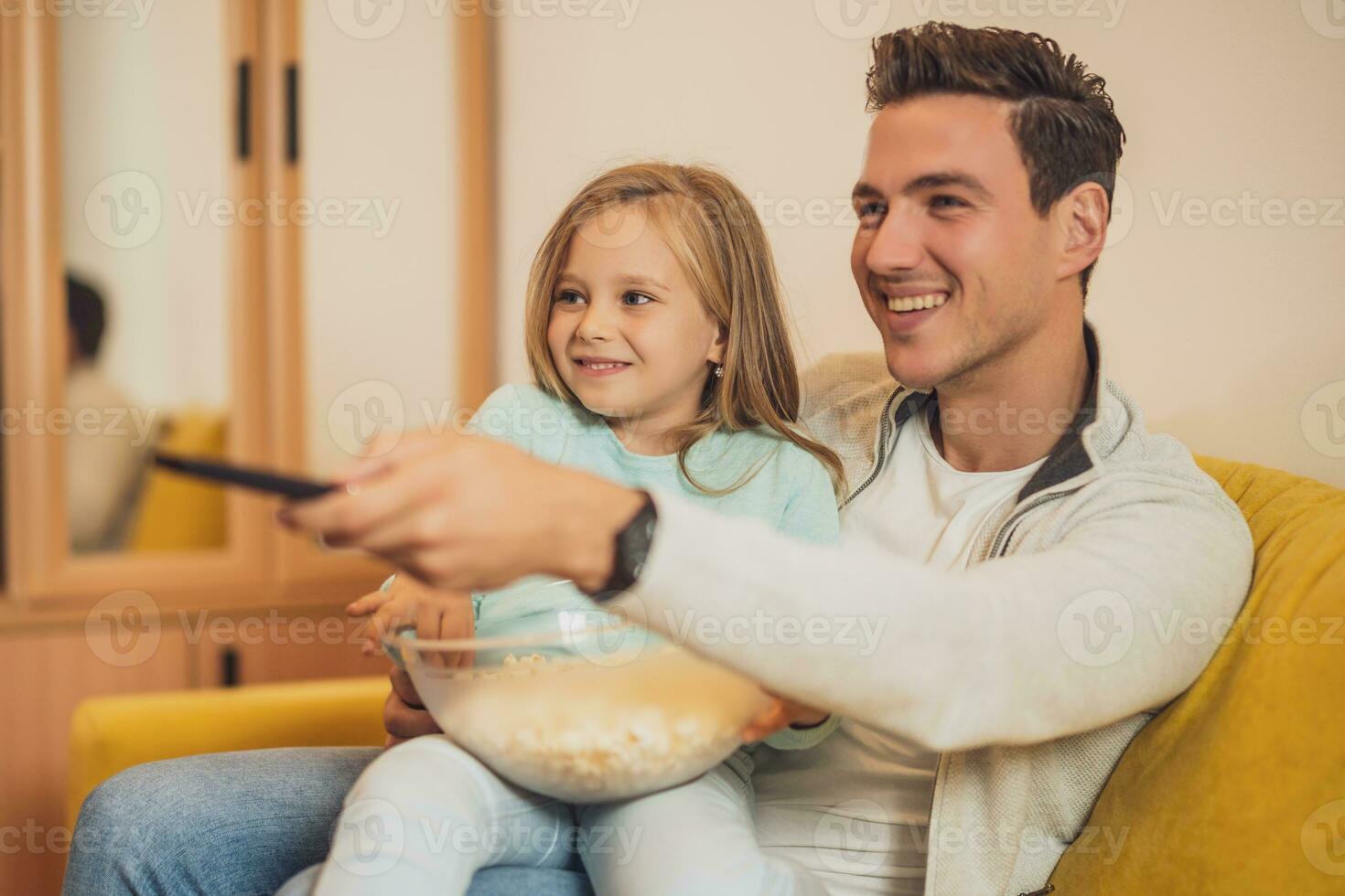 Father and daughter enjoy watching tv and eating pop corns together at their home photo