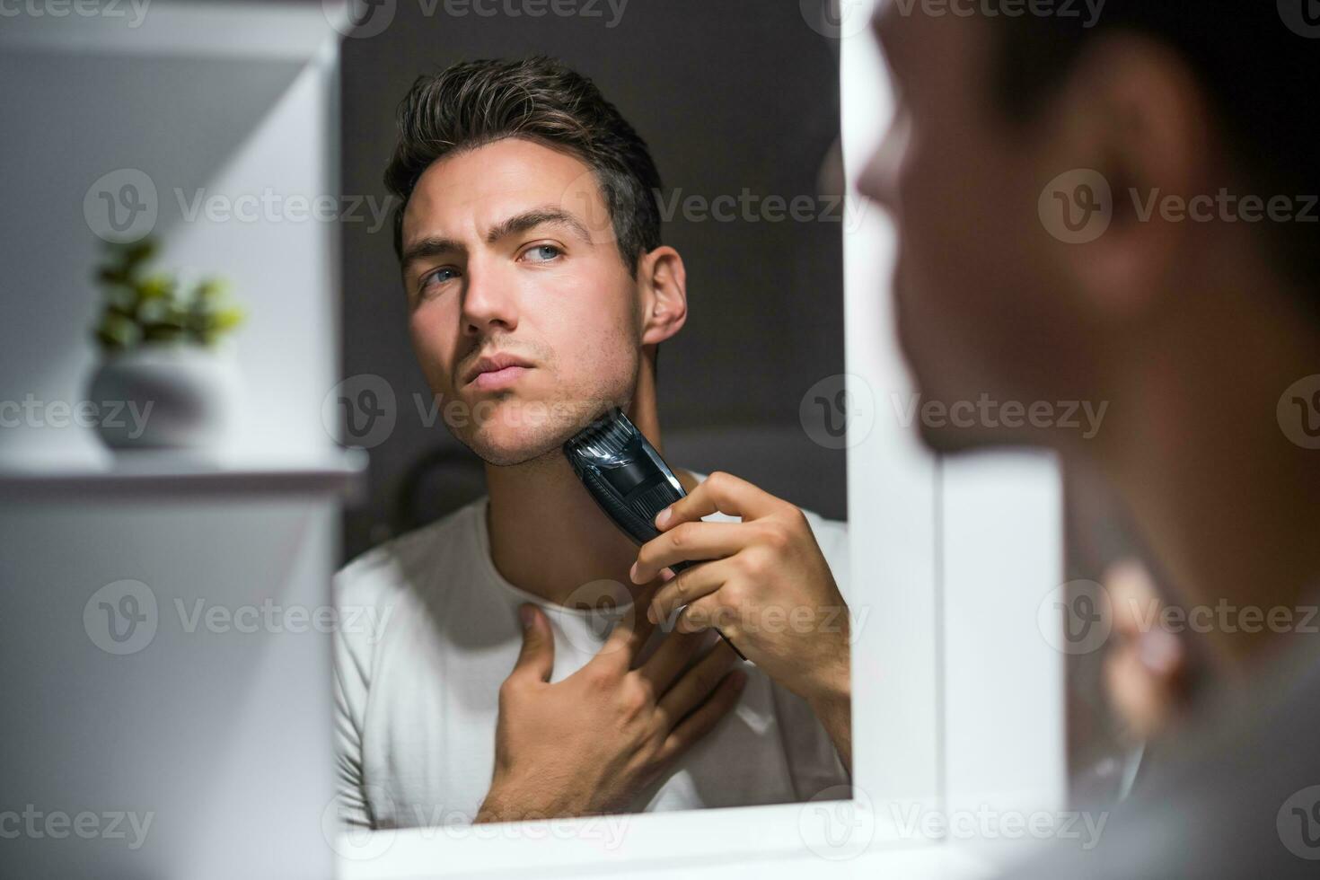 Man shaving  beard while looking himself in the mirror photo