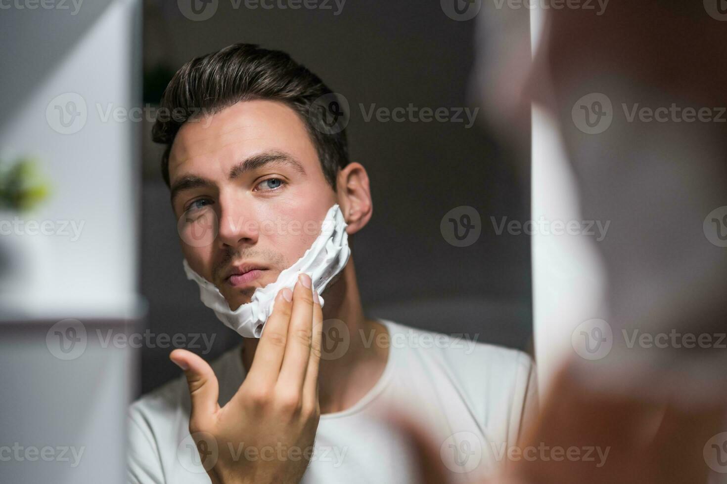 Man applying shaving cream while looking himself in the mirror photo