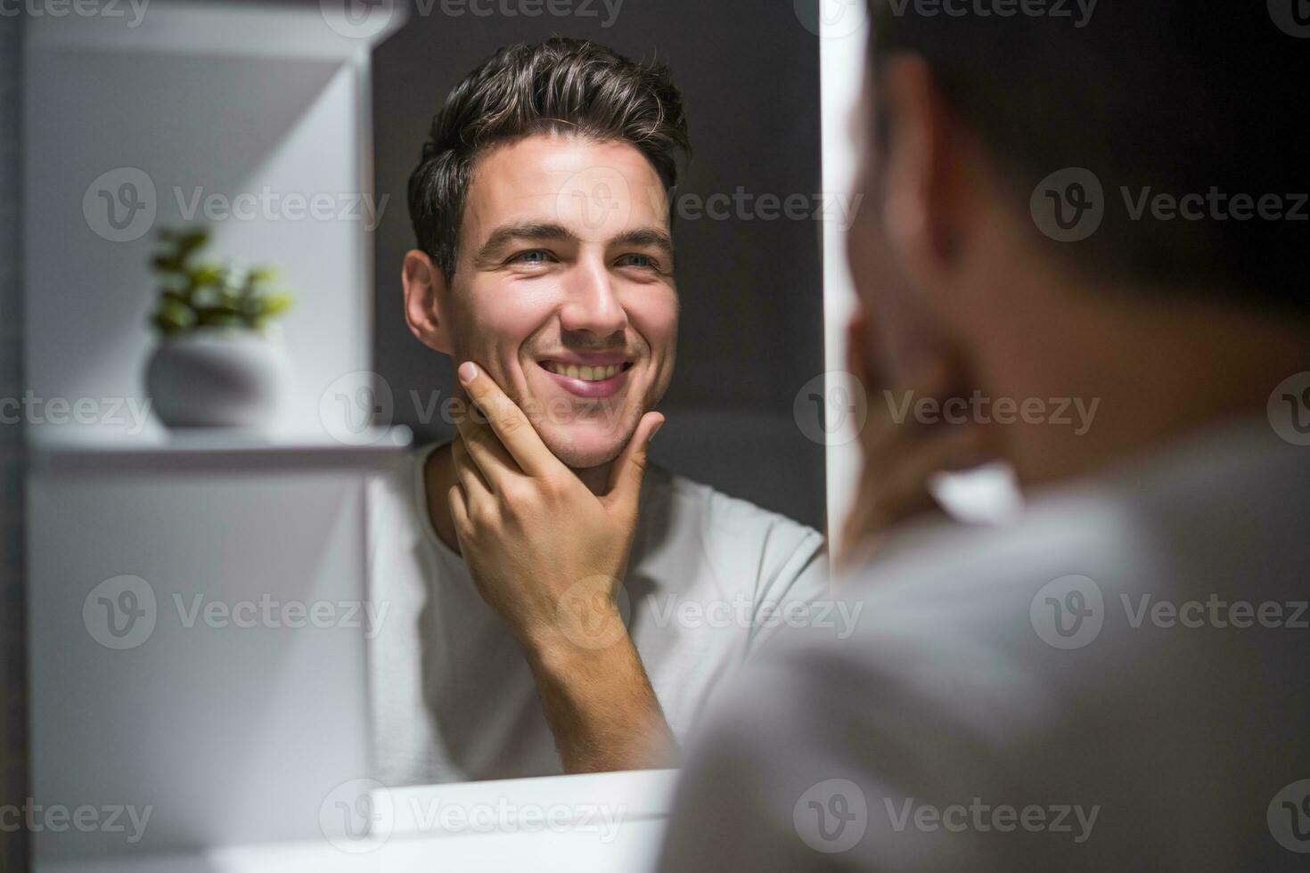 Portrait of man looking himself in a mirror while standing in bathroom photo