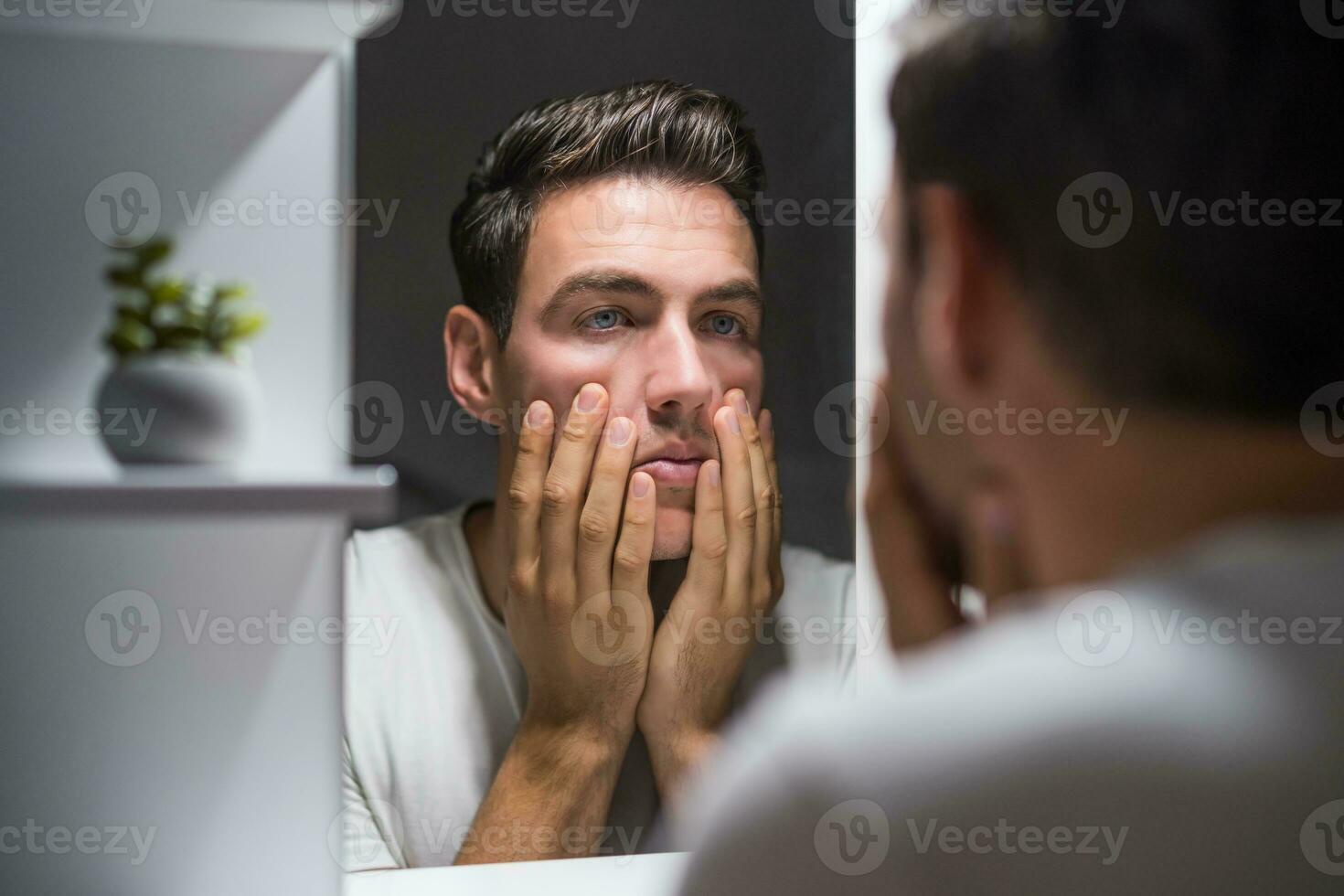 Man looking his eye bags in mirror photo