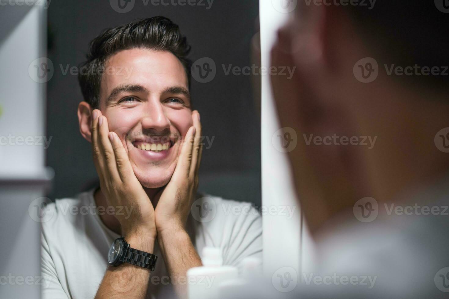 Man is applying aftershave while looking himself in the mirror photo