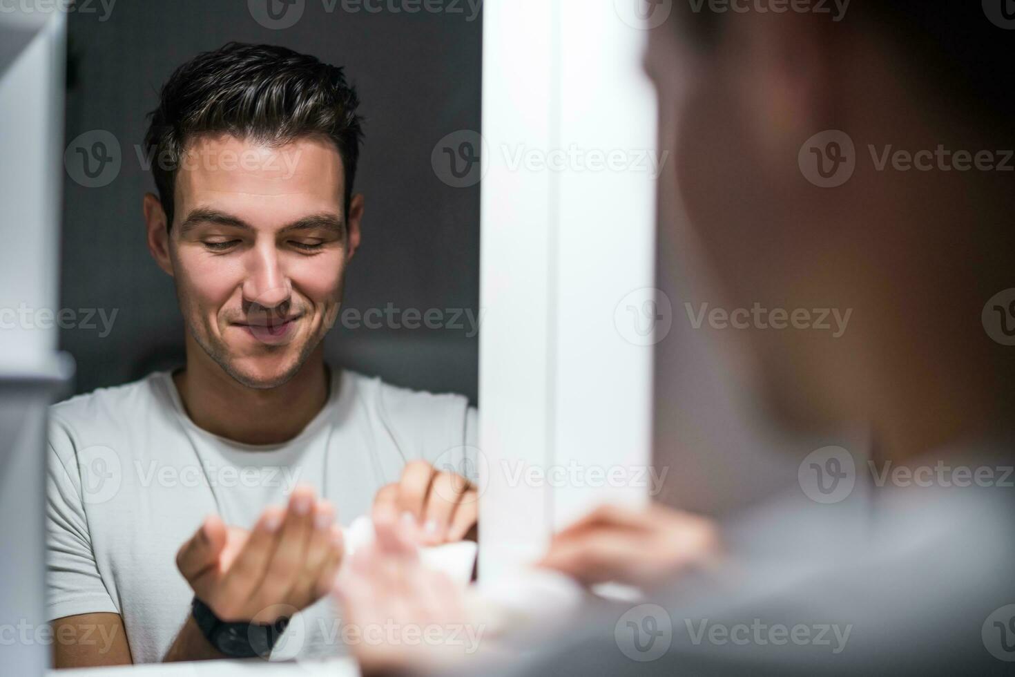 Man is applying aftershave while standing in front of mirror photo