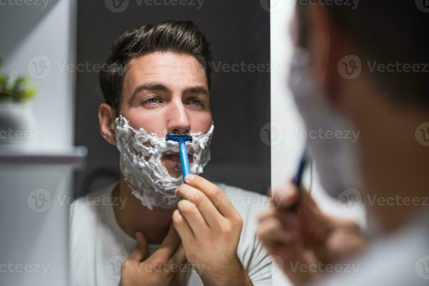 hombre afeitado barba mientras mirando él mismo en el espejo foto