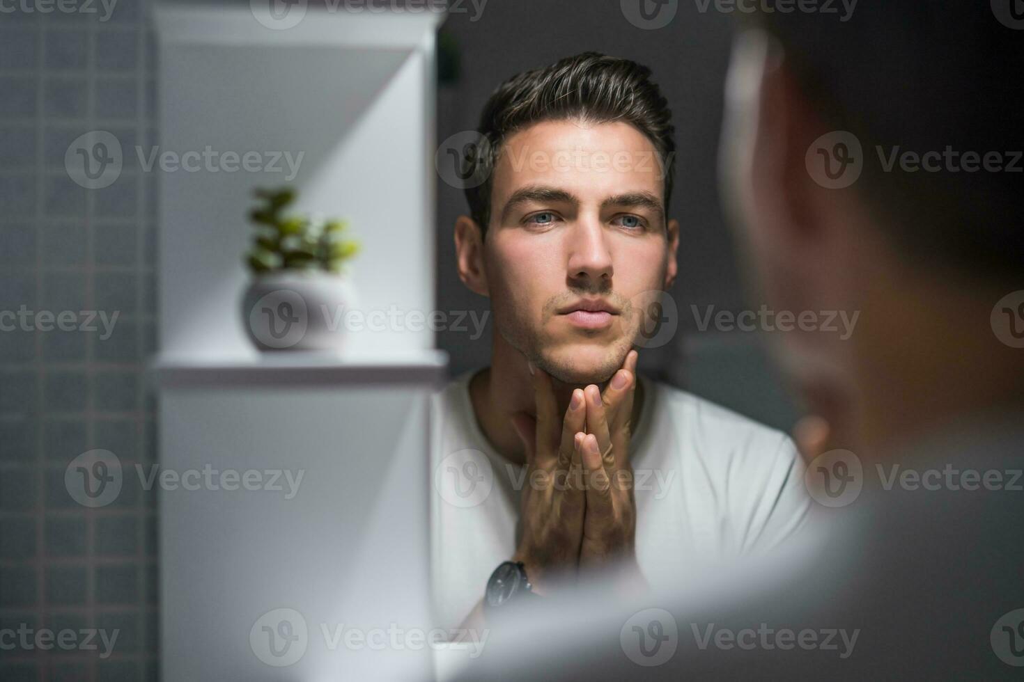 Portrait of man looking himself in a mirror while standing in bathroom photo