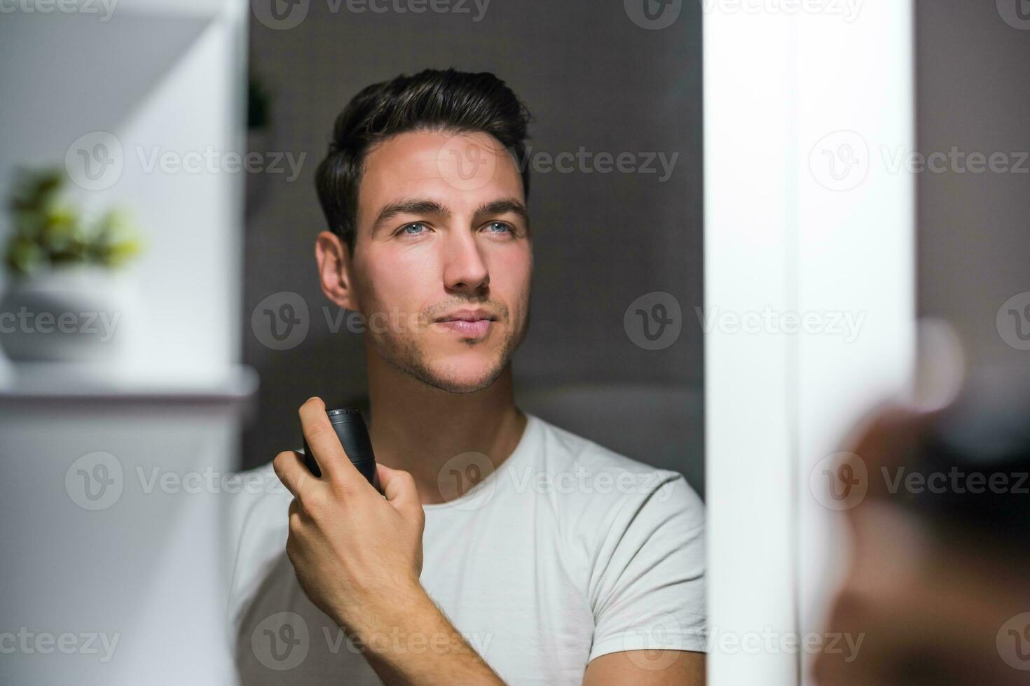 Man using deodorant while looking himself in the mirror photo